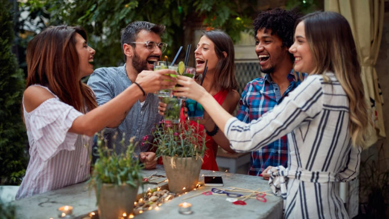 Group of cheerful friends making a toast at cafe's garden with cocktail drinks