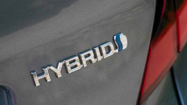 Stock Photo ID: 1743841019. Closeup of Hybrid sign on grey toyota car parked in the street. Hybrid emblem on a vehicle. EV, electric vehicle, grey and silver car, automobile, green, energy, conservation.