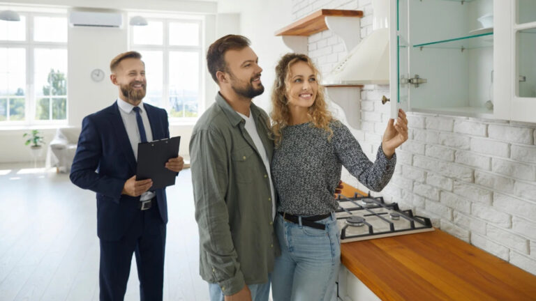 A male realtor leads a young couple through a new home tour