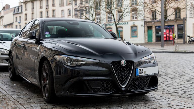 Front-side view of an all black Alfa Romeo Giulia Quadrifoglio parked on the side of a small brick street.
