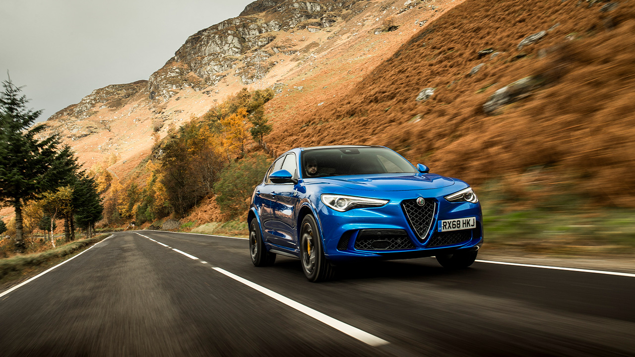 Alfa Romeo Stelvio Quadrifoglio, front 3/4 view, driving, blue, mountain road.