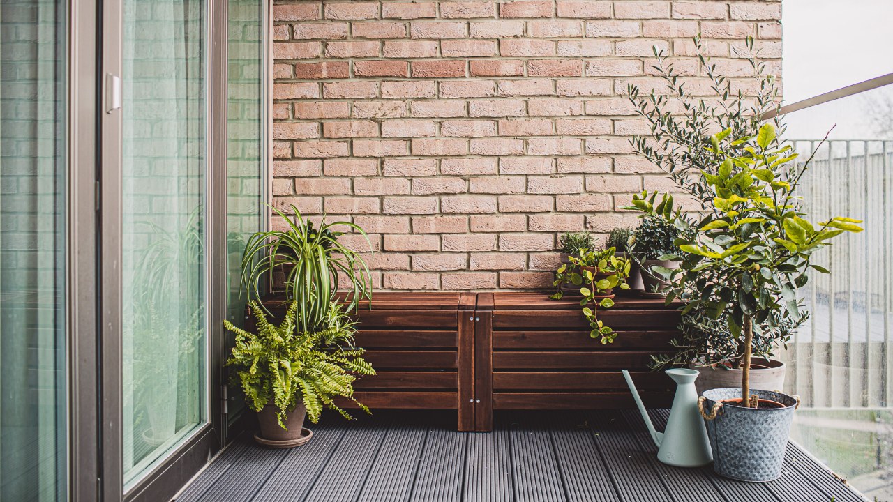 Morden residential balcony garden with bricks wall, wooden bench and plants.