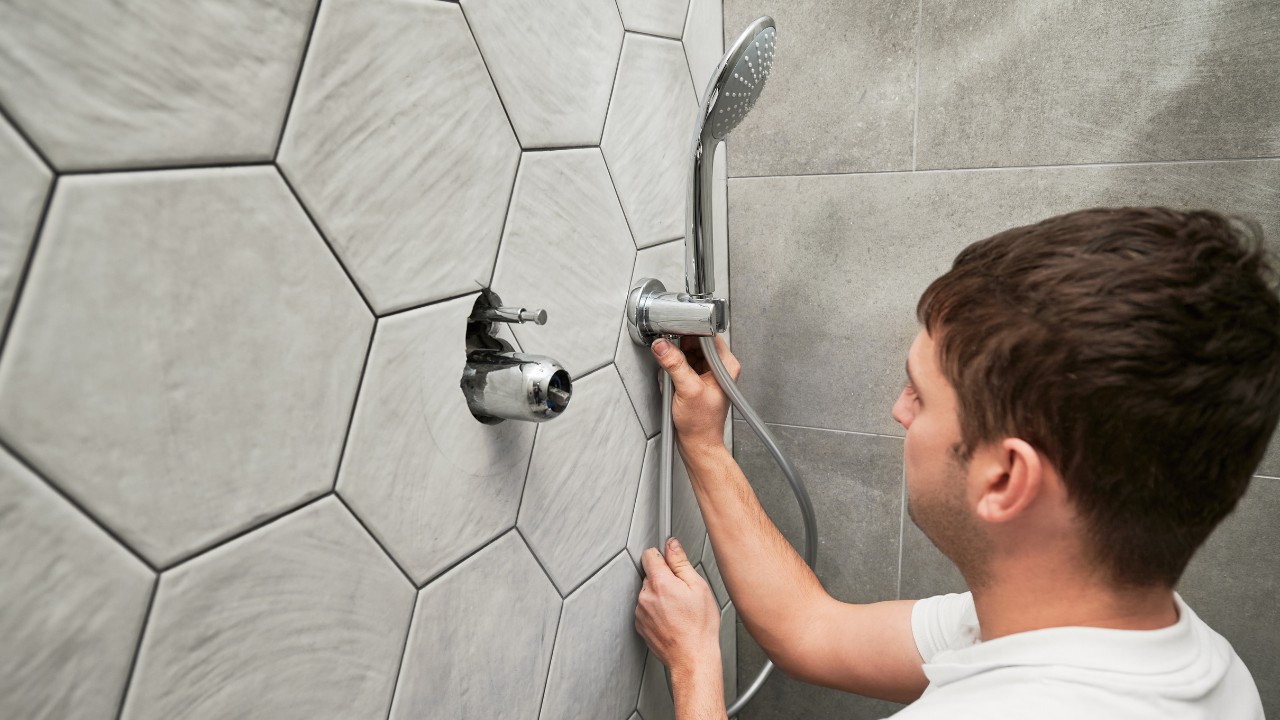 Male worker fixing metal bath showerhead and doing plumbing works while working on home renovation.