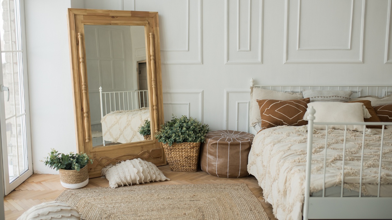 Bright and spacious bedroom with a white wall, an eco-wooden mirror and flower pots. Cozy bright rustic style bedroom, boho style bedroom.