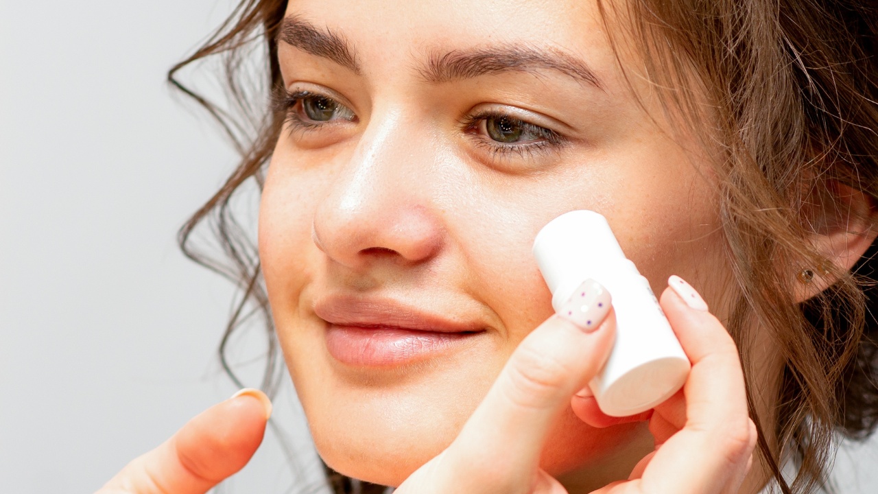 Makeup artist applying cream blush foundation tube on the cheek of the young woman in a beauty salon.