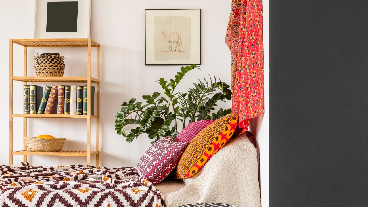 Cozy bohemian-style bedroom complete with tapestries, a variety of textiles, books, hanging art work, wooden furniture and pillows. 