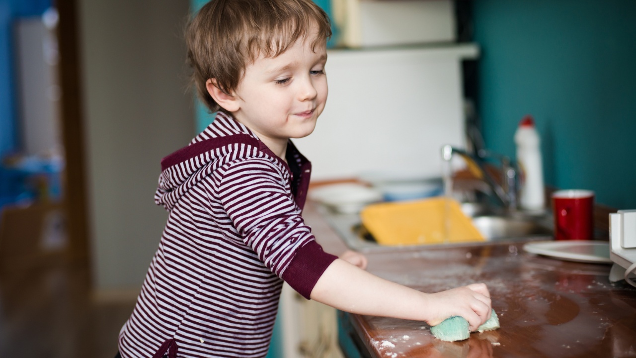 A young boy cleaning kitchen countertops and smiling.