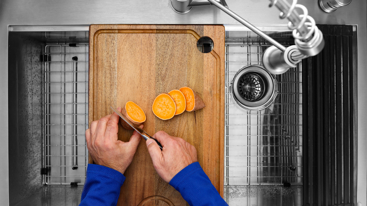 Chopping a sweet potato or yam on a cutting board over a multipurpose or workstation sink