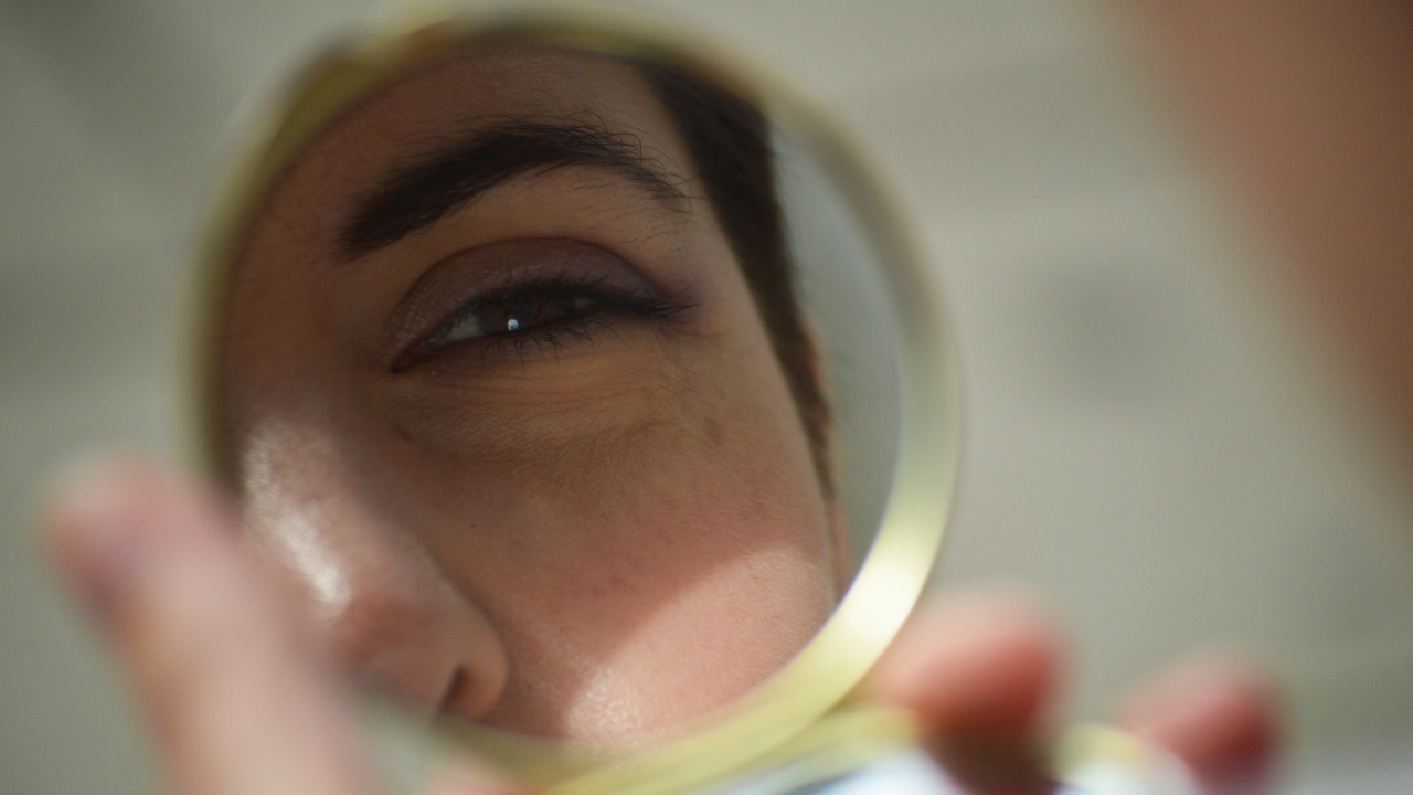 A woman looking into a small golden compact mirror. You can see her eye and brow in the reflection.
