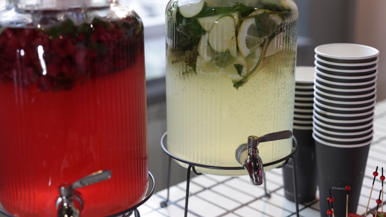 A close-up photograph of two large glass beverage dispensers placed on a countertop, each filled with refreshing, infused drinks.
