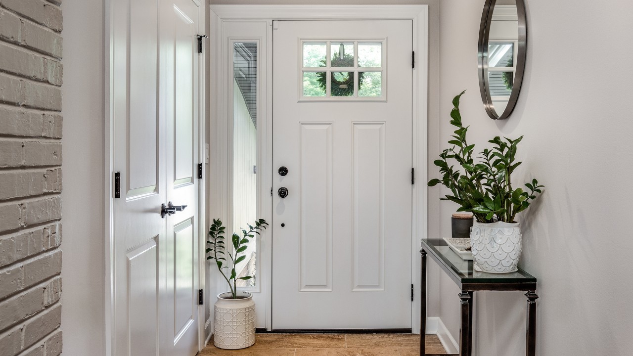 A cozy entryway with brown and brick walls, hardwood flooring, decorations, and a white front door with windows.