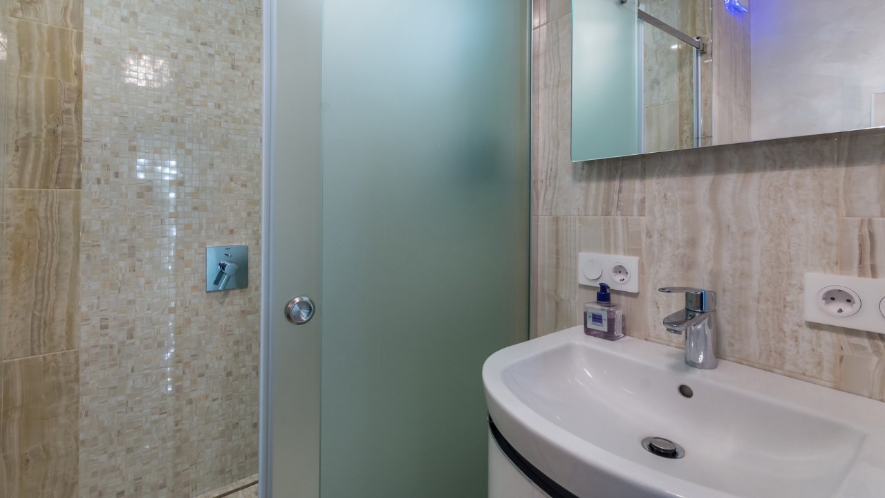 A small bathroom decorated with beige tiles. Frosted glass shower door.