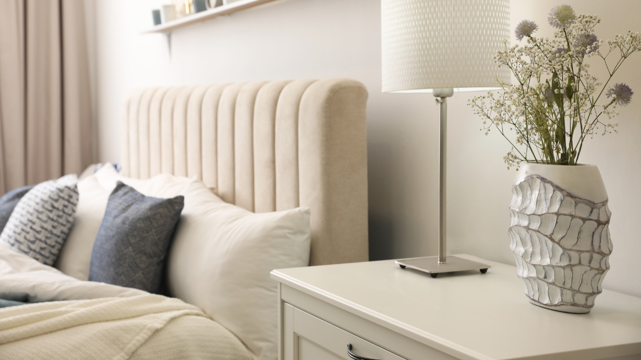 Front-side view of a cream color bedroom set, with focus on the headboard and side table lighting. 