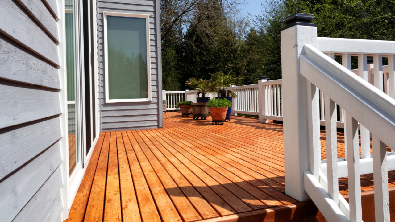 Freshly stained walk out home outdoor cedar wood deck with potted plants in bloom.