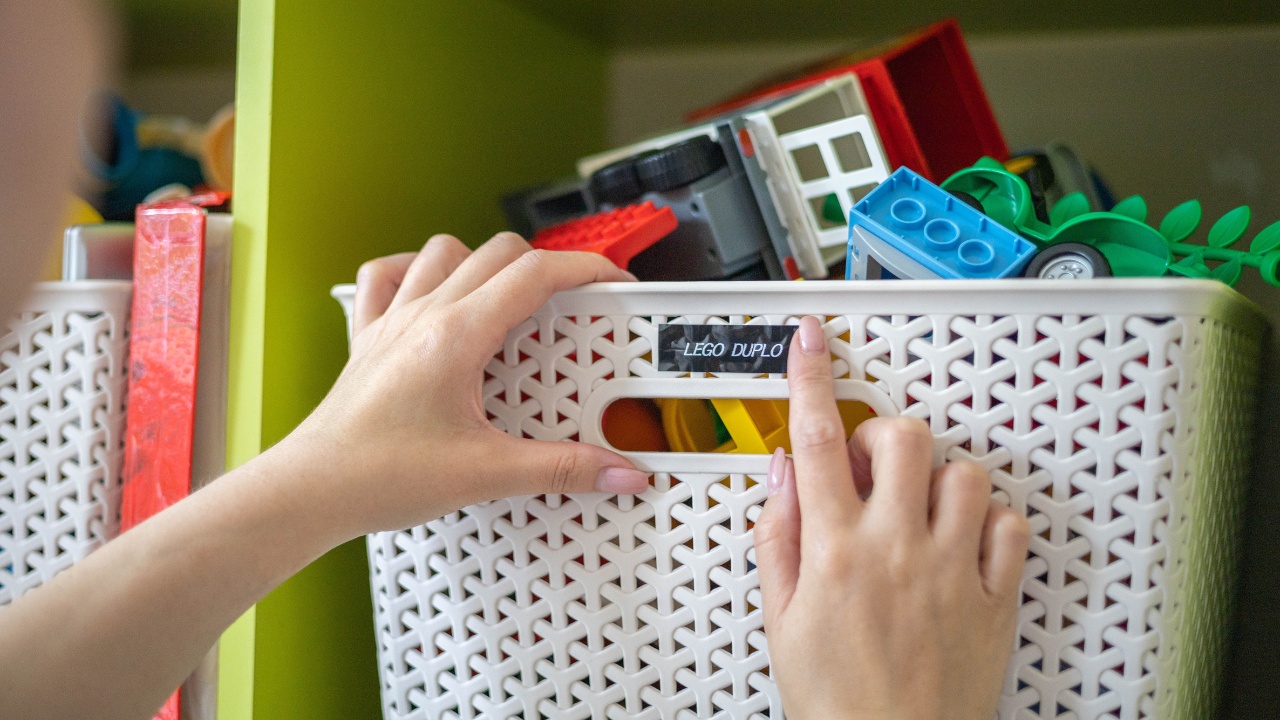 A woman presses a label on a basket full of Lego and Duplo toys after organizing it.