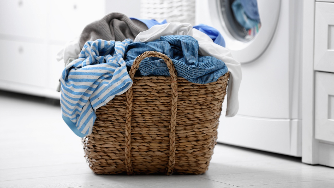 Wicker basket with dirty laundry on floor in front of washing machine. 