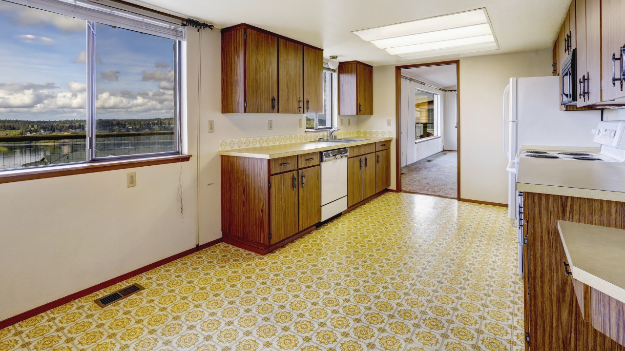 Empty kitchen room with linoleum floor, old storage cabinets and white appliances. 