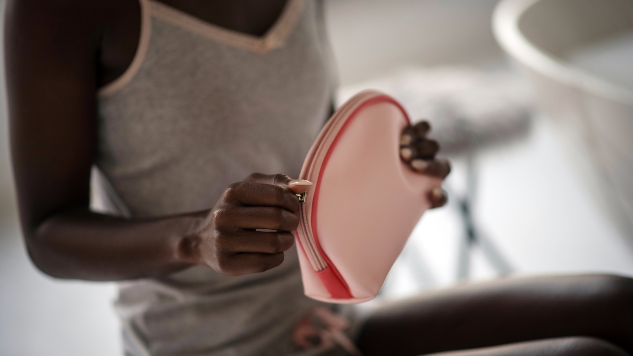 A woman sitting and zipping closed a pink cosmetic bag/makeup bag.