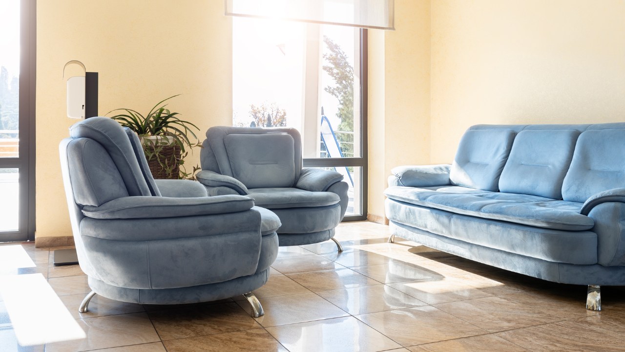 Sunlit, cozy lounge corner featuring plush blue armchairs and a matching sofa.