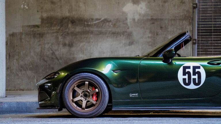 Green Mazda Miata MX-5 parked on the curb under a bridge on 4th street. Car has a number on the side.