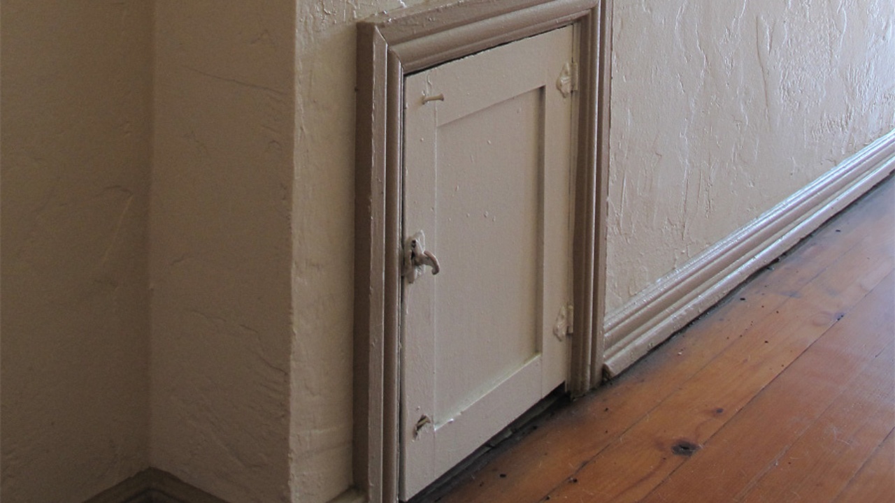 Milk delivery door, or package safe, in hallway outside 1920s apartment in Los Angeles, California. This is a small wooden cabinet on the inside of the apartment, built into the exterior wall, with doors on both sides. A delivery of milk or groceries could be placed in the box from the outside when the owner was not home. Both sides are latched but not locked.