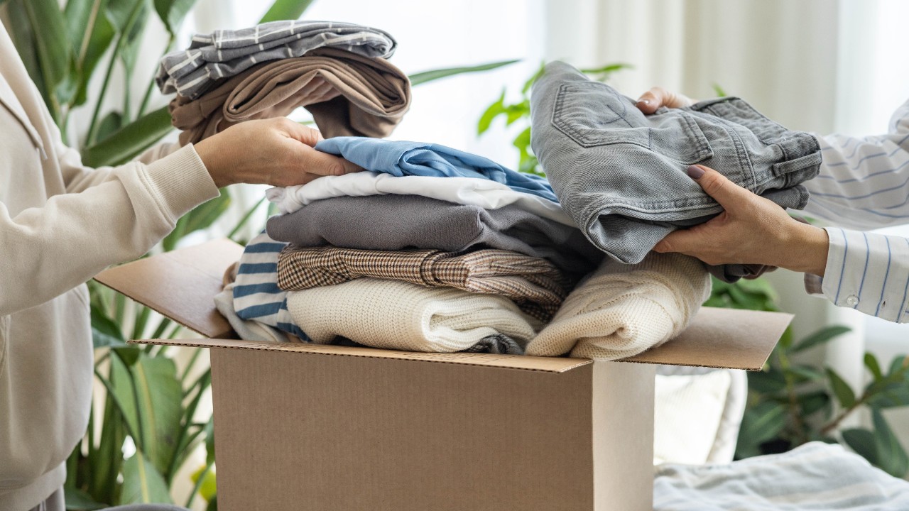 Two women organize clothing in a box either for storage or donations.