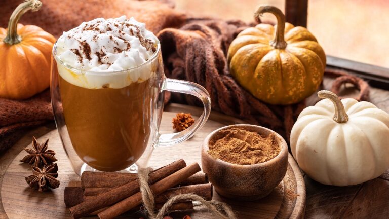Pumpkin spice latte with cinnamon sticks on a wooden platter and pumpkins by a window