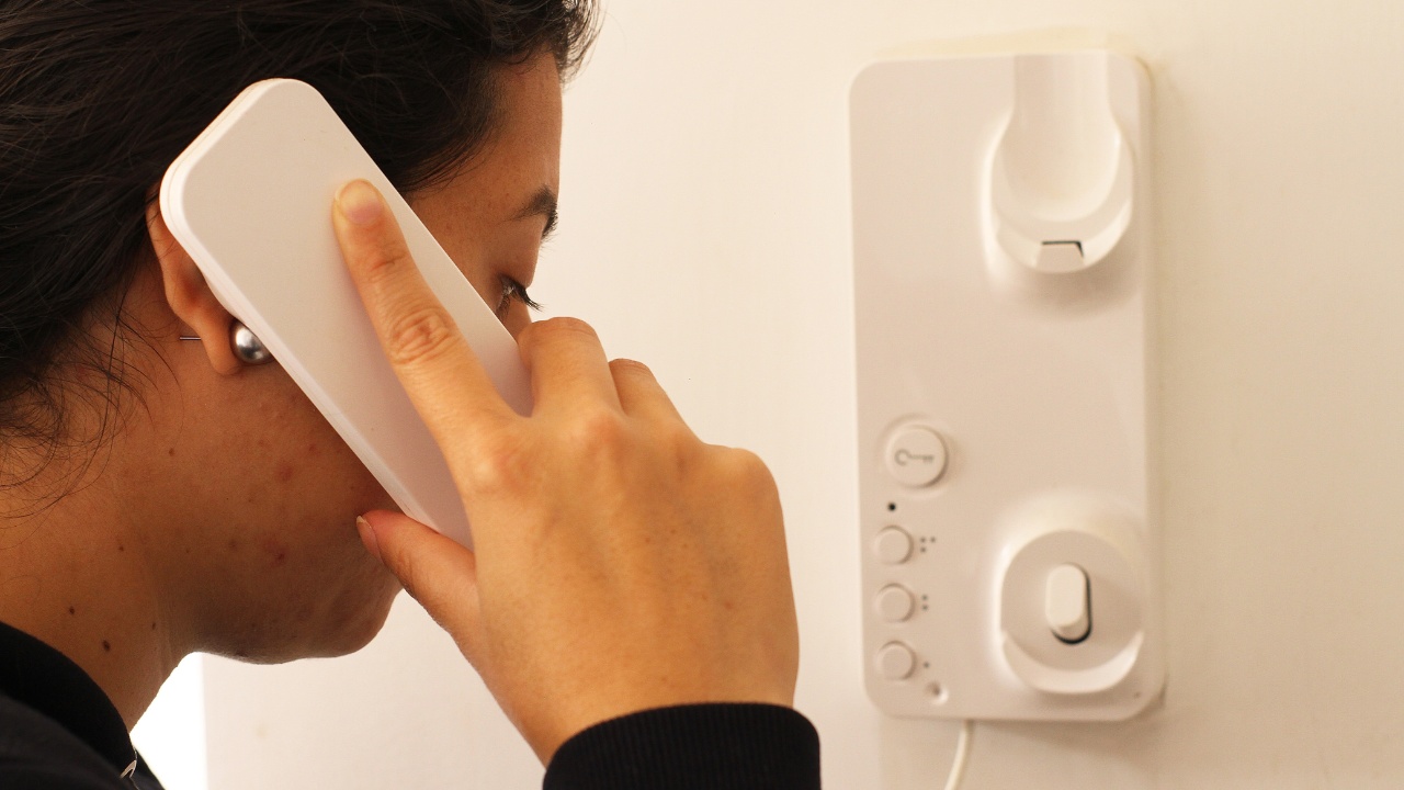 A woman answering and talking on a white intercom system telecommunication device.