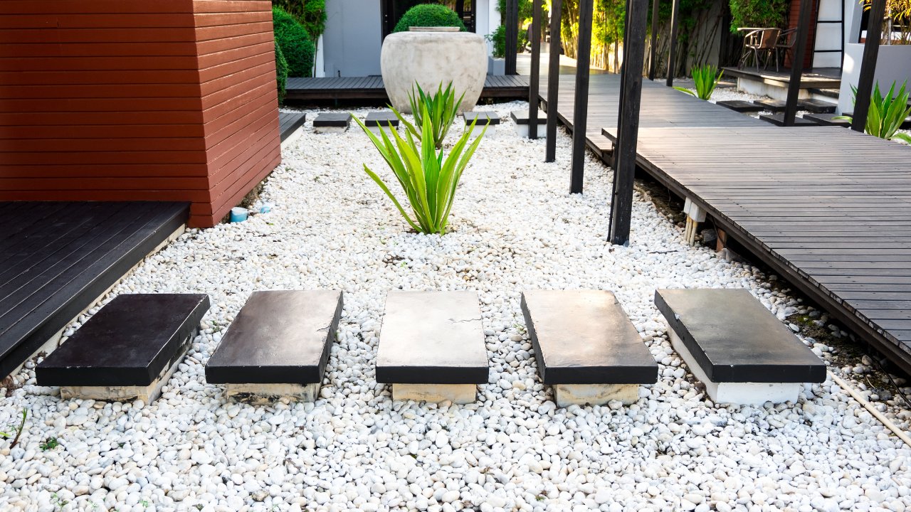 A black deck and modernized outdoor recreational area with potted plants and white rocks. 