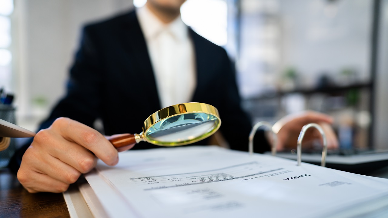 Person going through paperwork with a magnifying glass