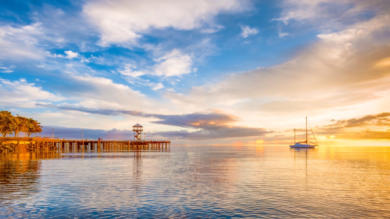 A boat anchored on the calm waters of the Puget Sound as the early morning sun rays warm the cloud ridden sky at Port Angeles, Washington