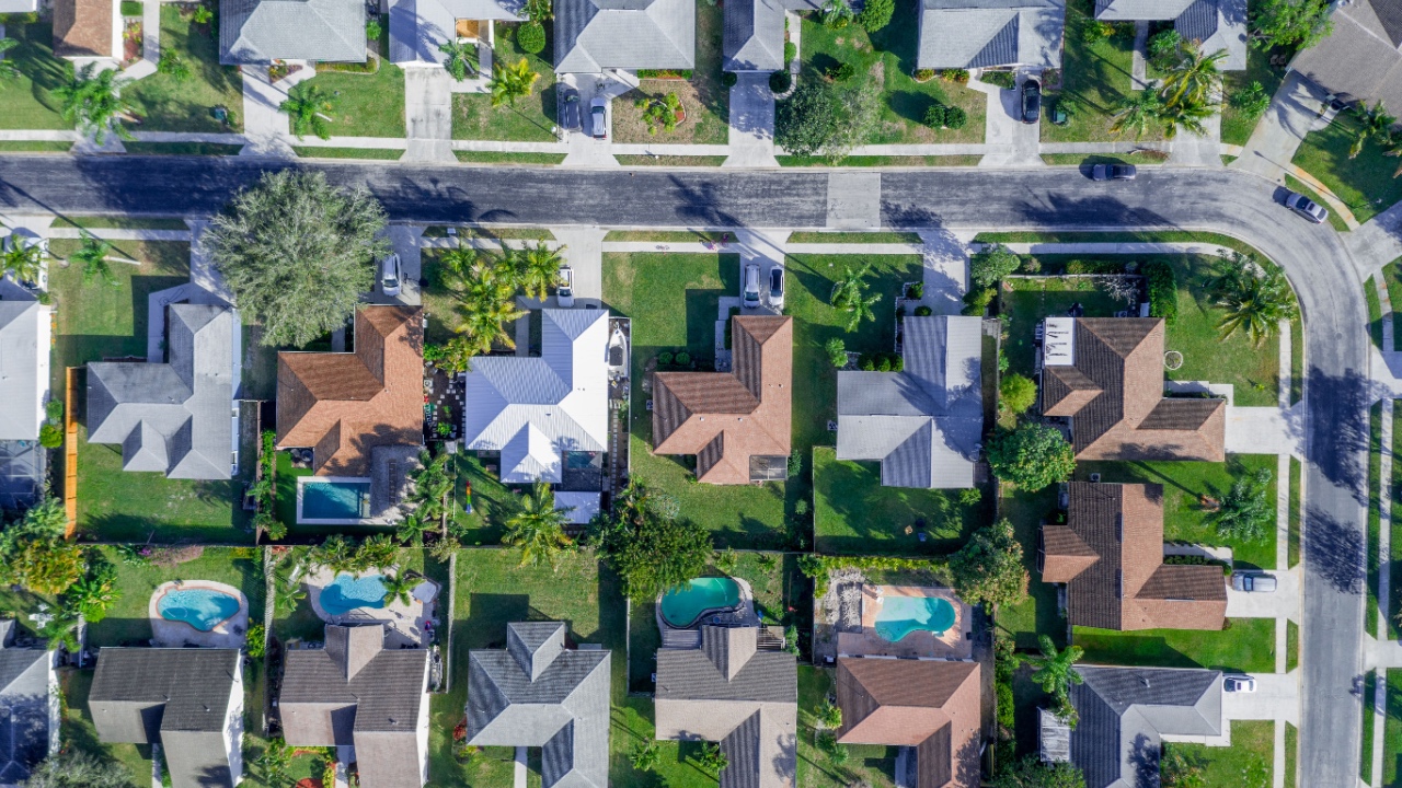 Aerial summer view of warm sunny neighborhood community roofs with horizontal streets and lots of houses with pools and palm trees.