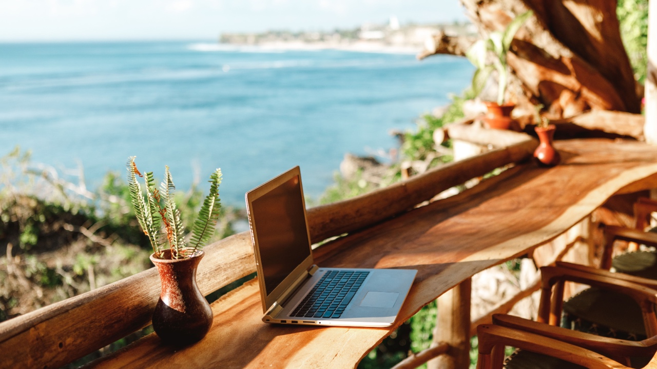 Open laptop with black screen on wooden table work space outdoors with amazing view on the ocean. Laptop on sea view backdrop. Bali.