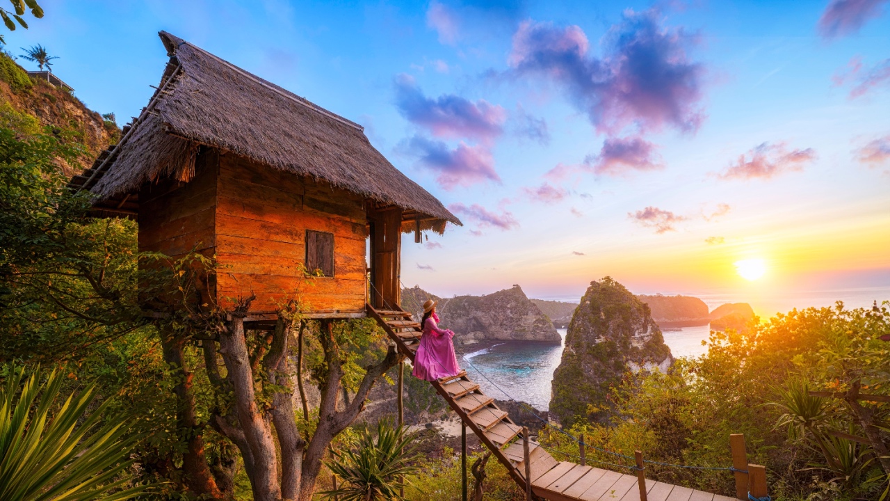 Happy and relaxed travel woman watching sunrise, tree house with diamond beach, Atuh beach in Nusa Penida island, Bali, Indonesia.
