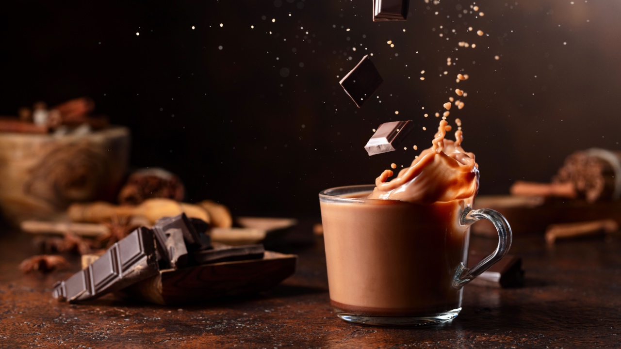 Pieces of dark chocolate fall into a glass of cocoa drink creating a beautiful splash.