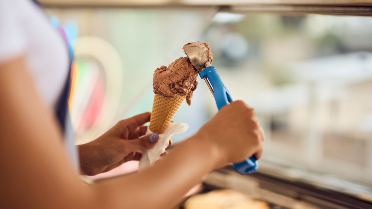 Close-up of a female putting a scoop of the ice cream on top of the cone.