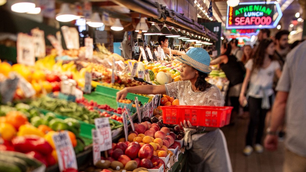 Woman stocking produce at farmers market stand Pike Place.