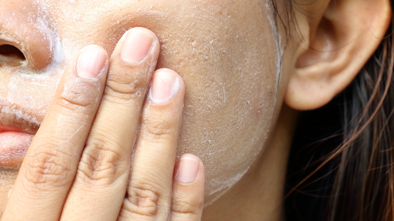 Close-up of a woman using skin care products (white foam) on her face.