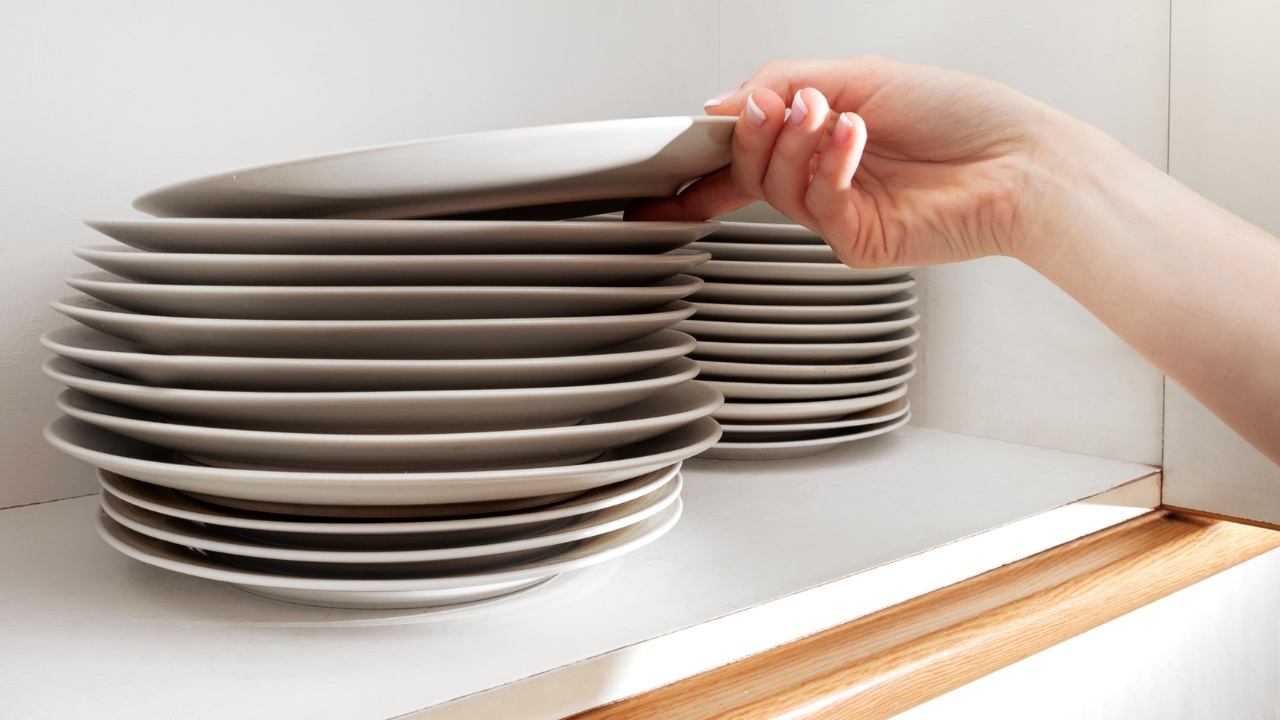 A feminine hand picking up a plate from a stack in the cupboard.