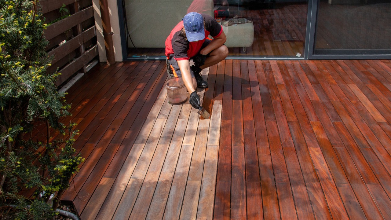 Wood worker applying nourishing deck oil with paintbrush on cleaned and sanded decking terrace boards.