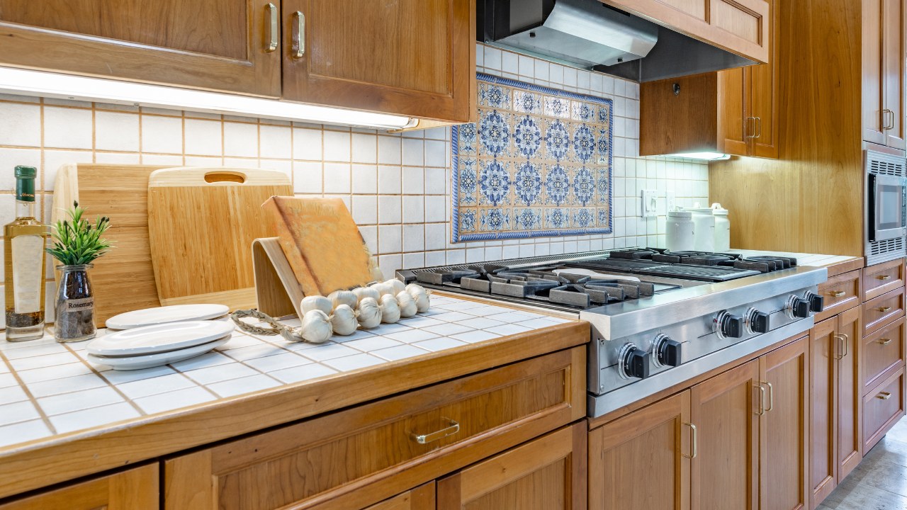 A spacious mid-century craftsman home kitchen with tiled countertops, white appliances, dining areas, bar stools, white pine-colored cabinets and mosaic backsplash.