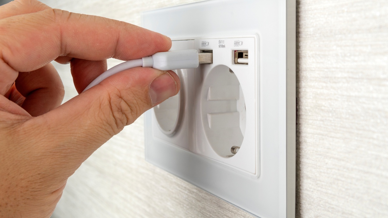 A masculine hand unplugging a USB plug from a wall outlet. 