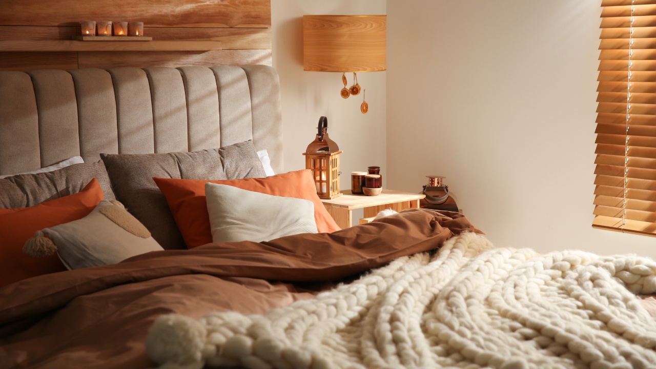Cozy bedroom interior with knitted blanket and cushions, candles, and other warm and inviting decor.