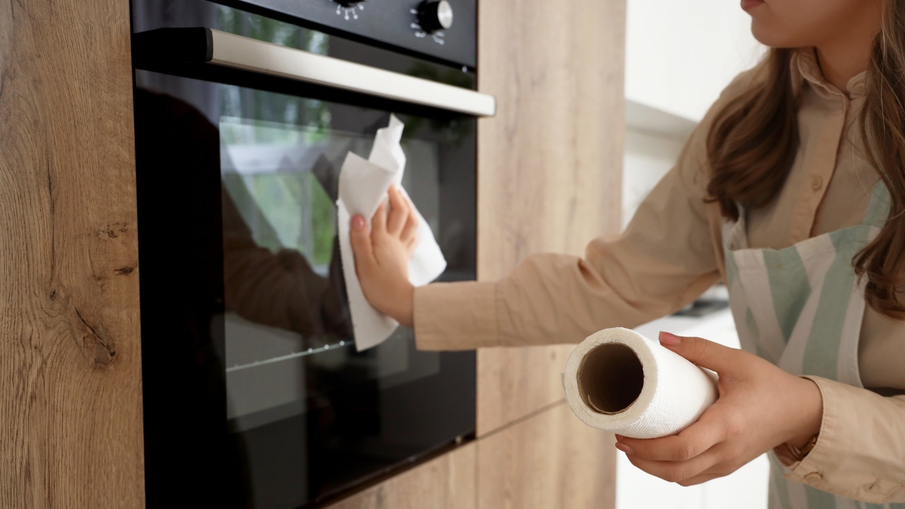 A woman wipes down the front exterior door of her oven.