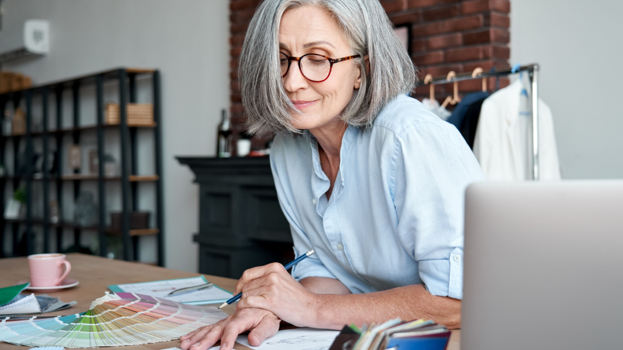 Middle aged stylish woman fashion designer drawing sketches in studio office. Mature old adult elegant grey-haired lady dressmaker small business owner creating new fashion design cloth in atelier.
