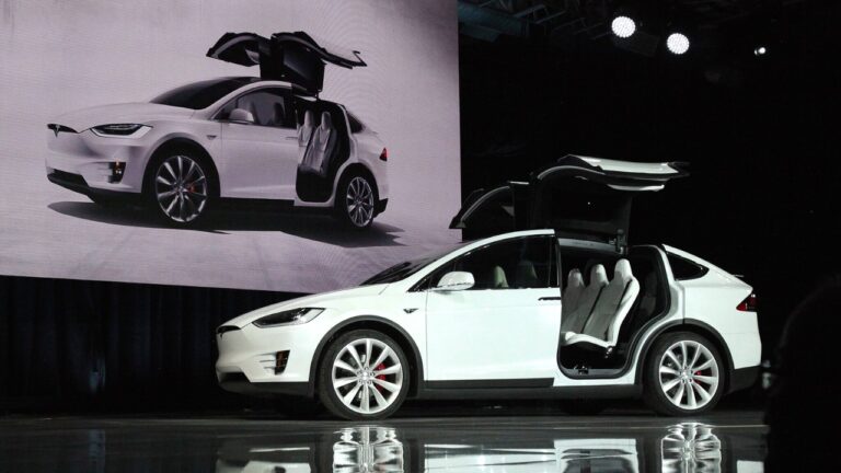 Front-side view of a white Tesla Model X at the market launch ceremony - the doors are open.
